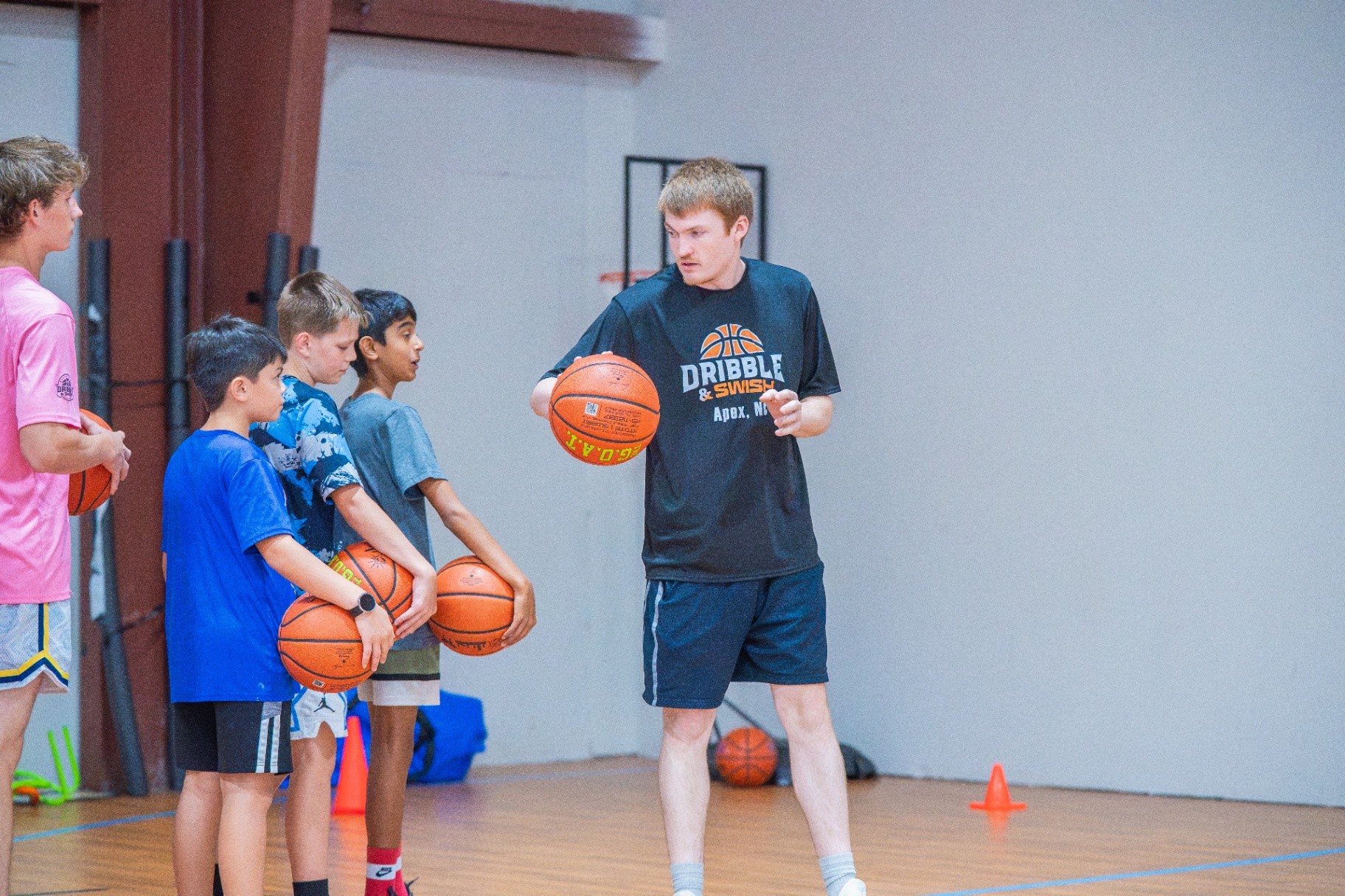 Coach demonstrating ball control for a line of athletes holding basketballs
