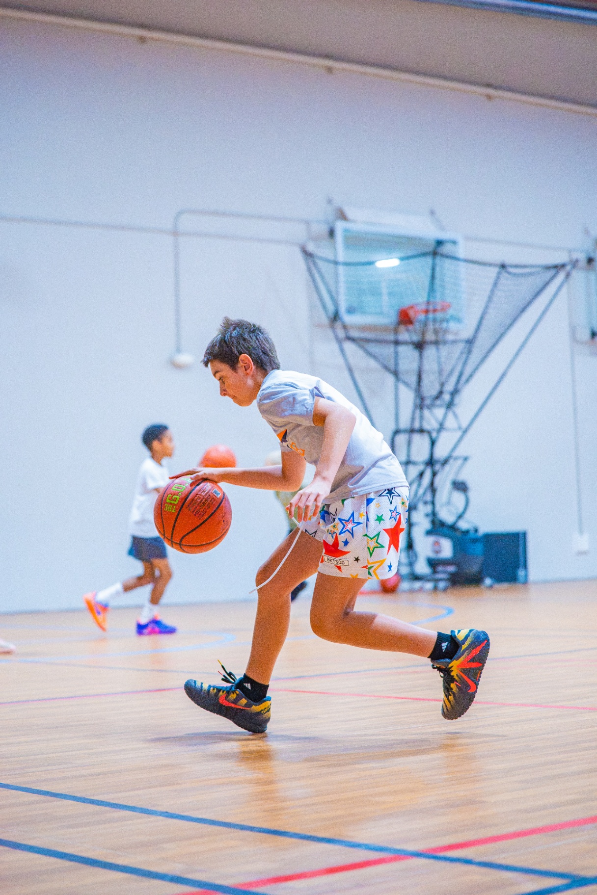 Young athlete in star-print shorts pushing the ball up the court in front of a Dr. Dish shooting machine
