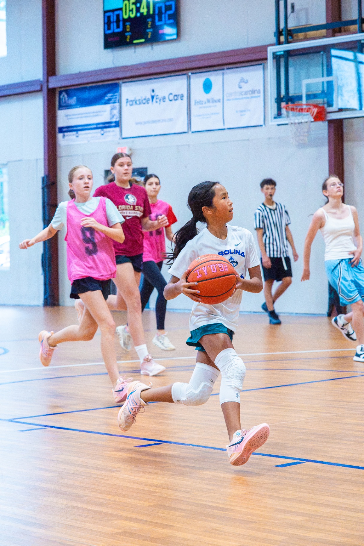 Athlete pushing the ball up the court on a fast break with teammates and defenders trailing