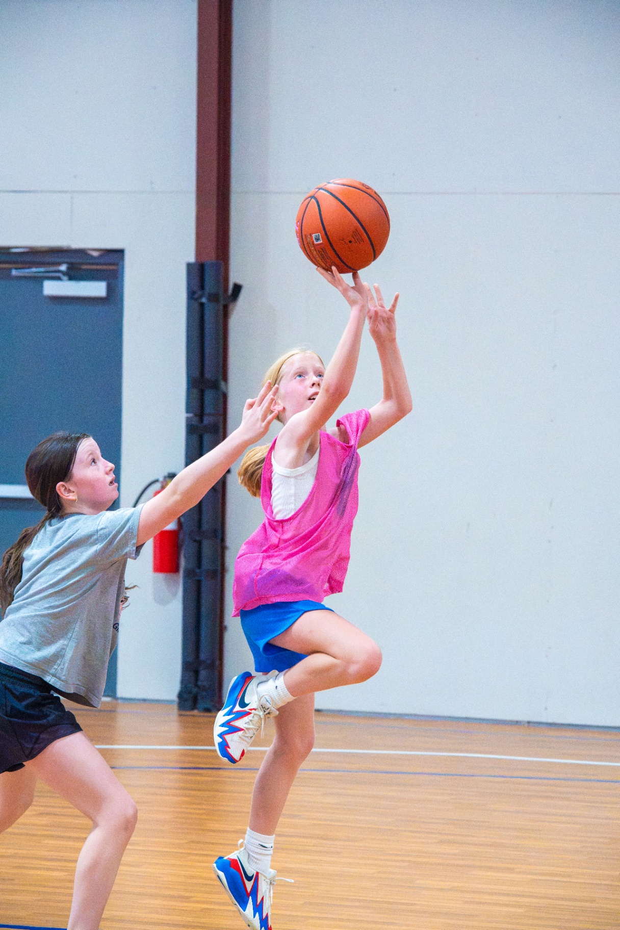 Player in a pink pinnie finishing a layup as a defender contests the shot