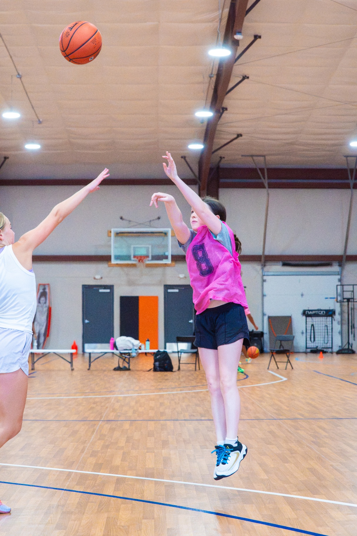 Player in a pink #8 pinnie rising up for a contested jump shot at center court