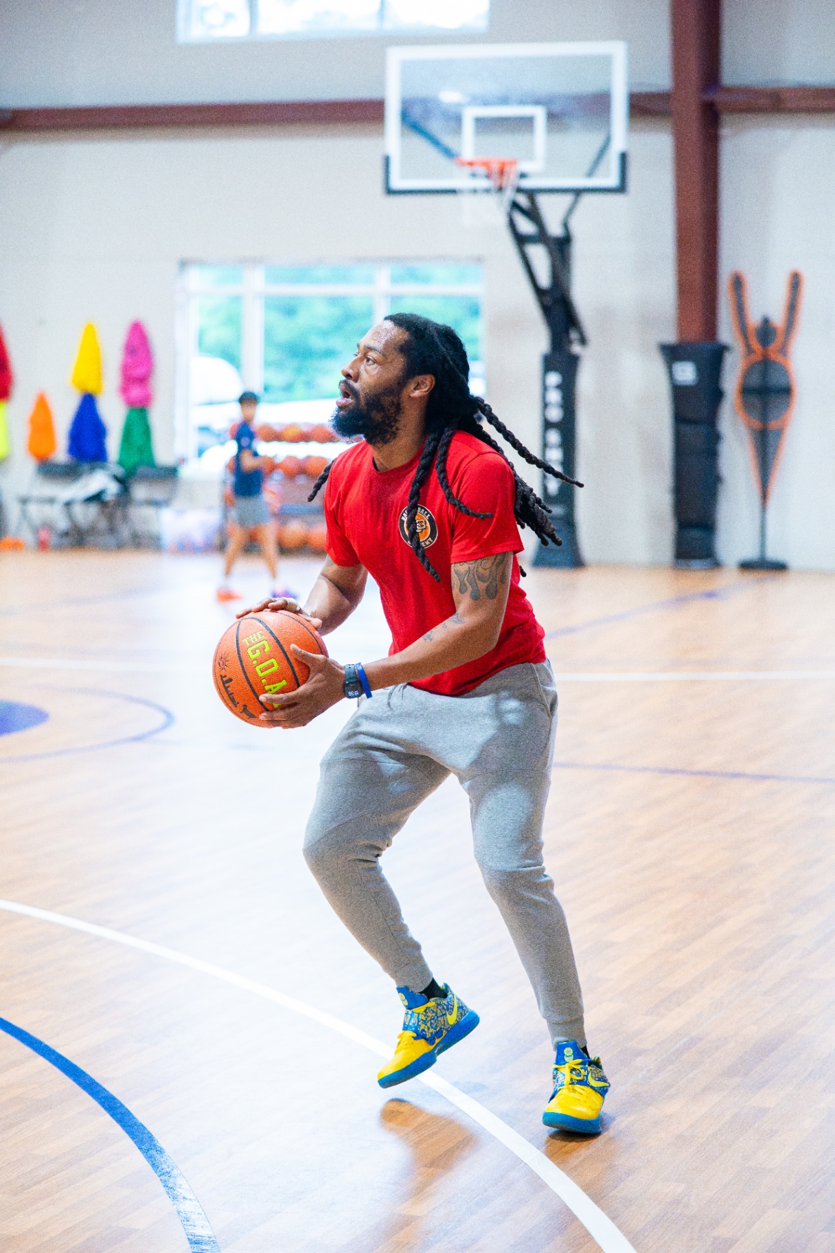 Coach in a red Dribble & Swish shirt loading up into a shooting stance at half court