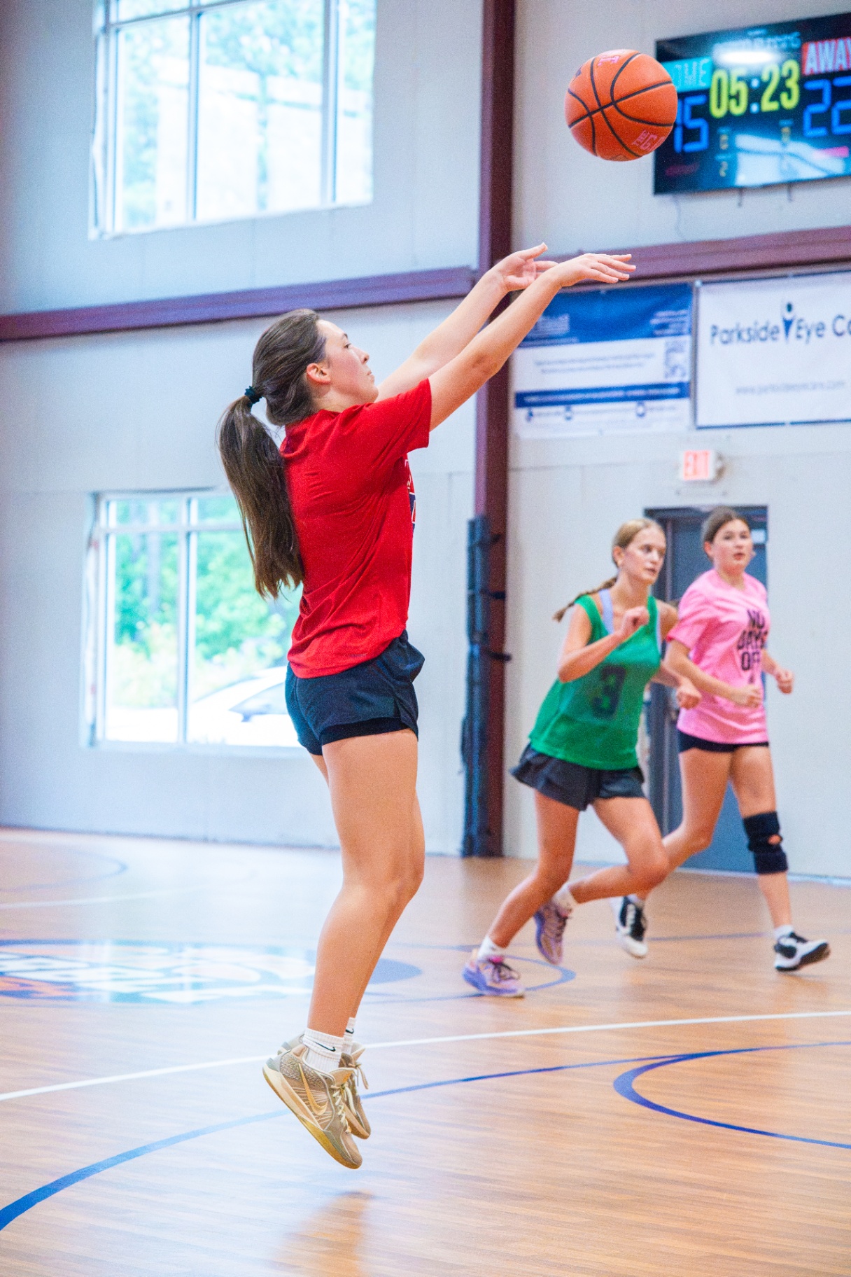 Athlete in a red shirt rising for a jumper on a fast break with teammates trailing