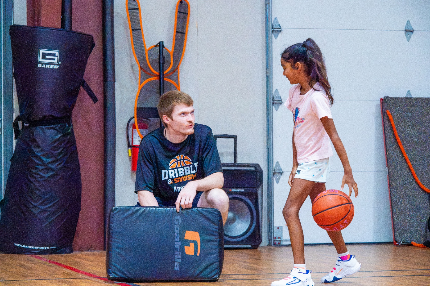 Coach kneeling beside a young athlete for one-on-one instruction during a Saturday session