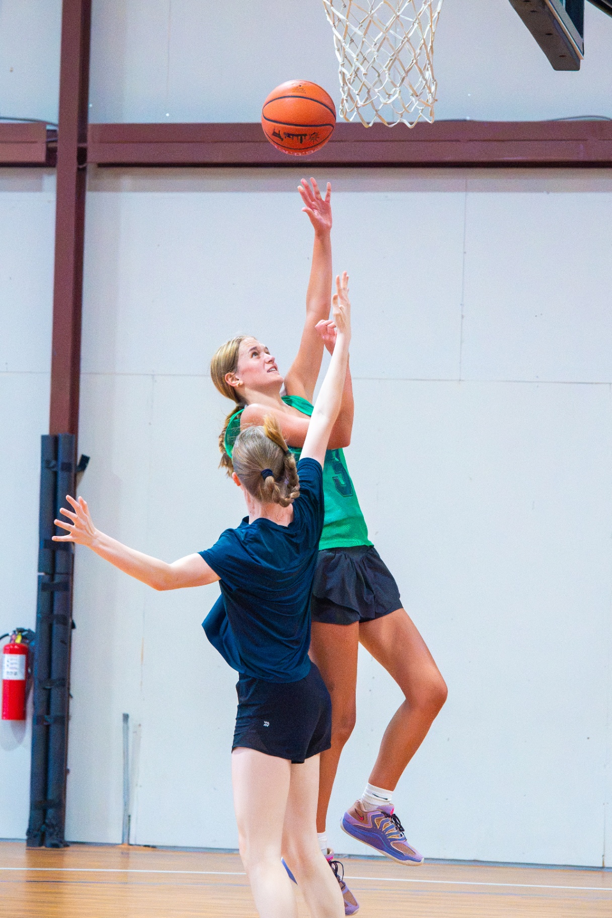 Athlete in a green pinnie elevating for a layup as a defender contests at the rim