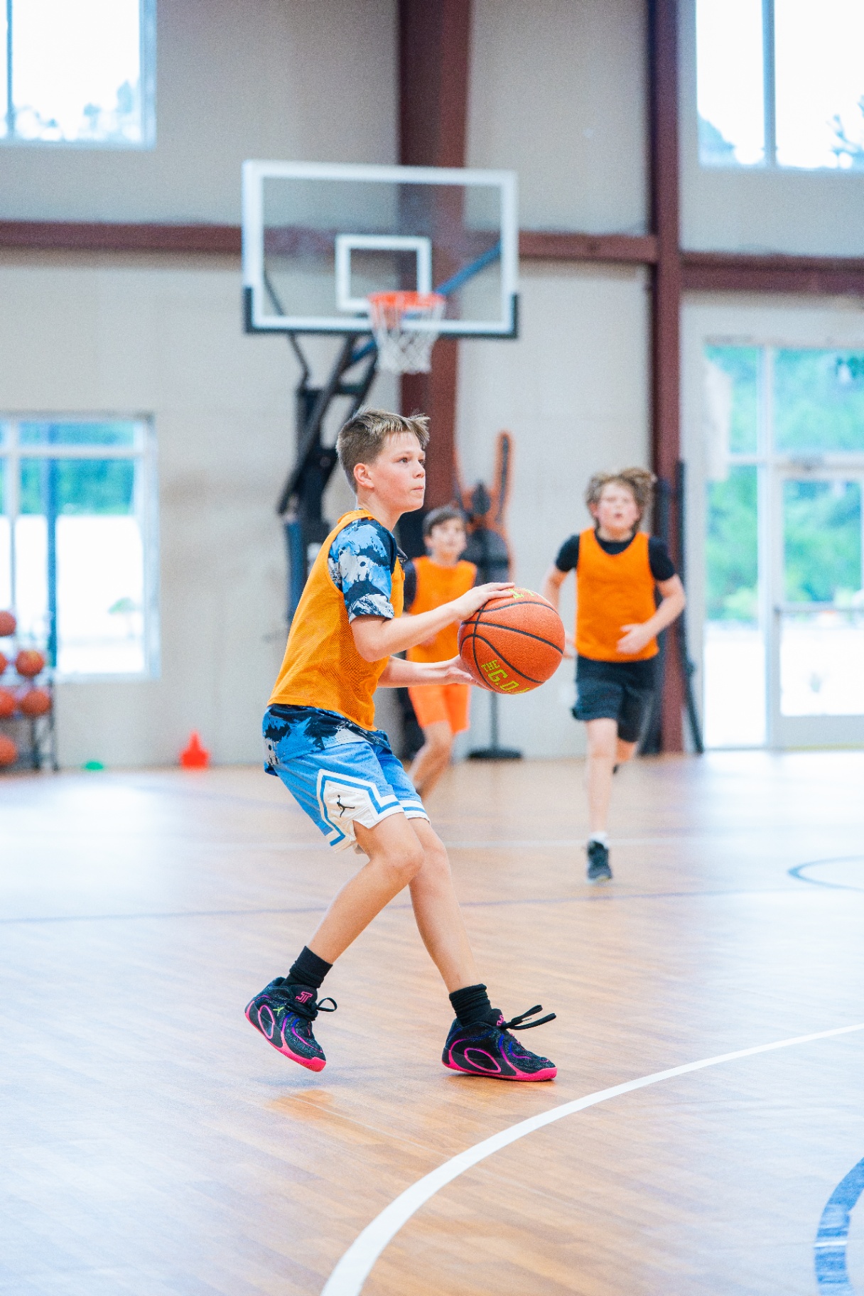 Young athlete in an orange pinnie squaring up to shoot as teammates sprint back on defense